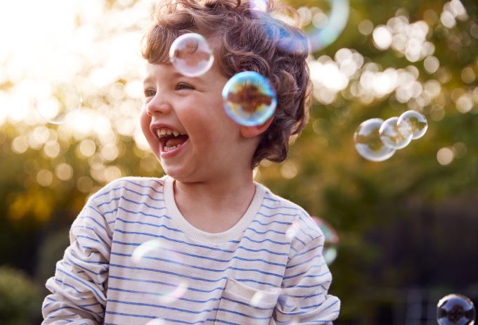 Young Boy Having Fun In Garden Chasing And Bursting Bubbles