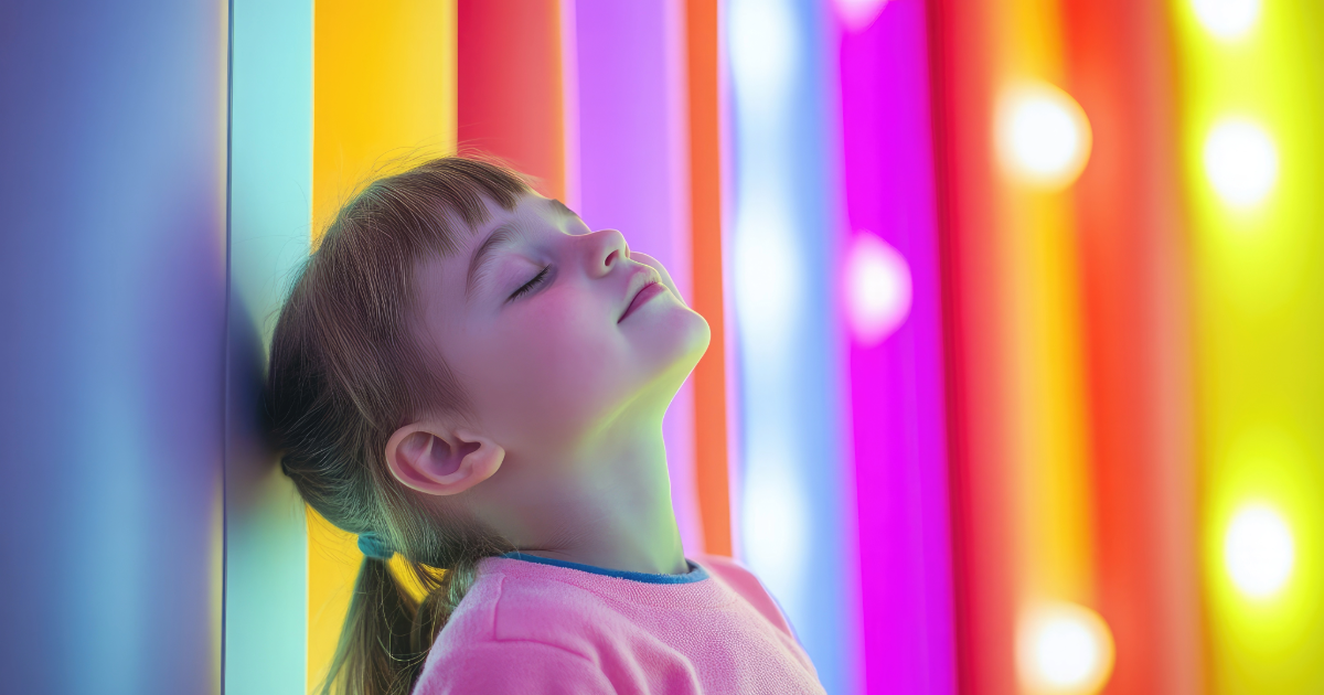 Girl leaning against brightly coloured wall. Eyes closed, smiling