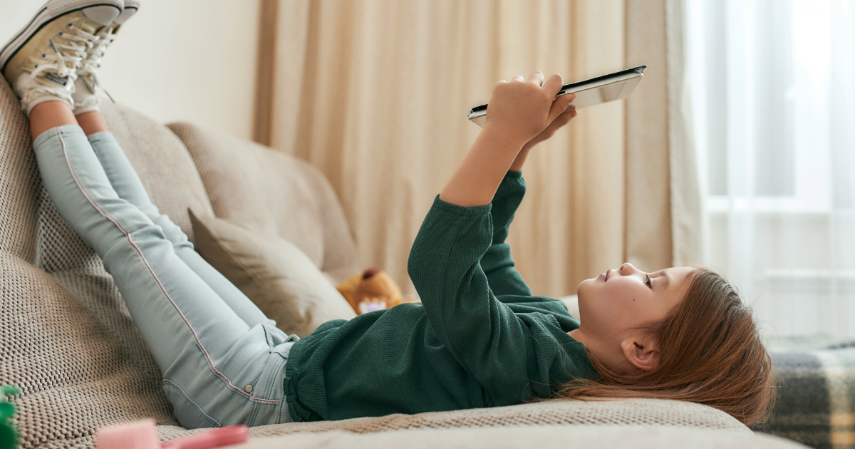 Child lying down with their legs up, looking at a tablet