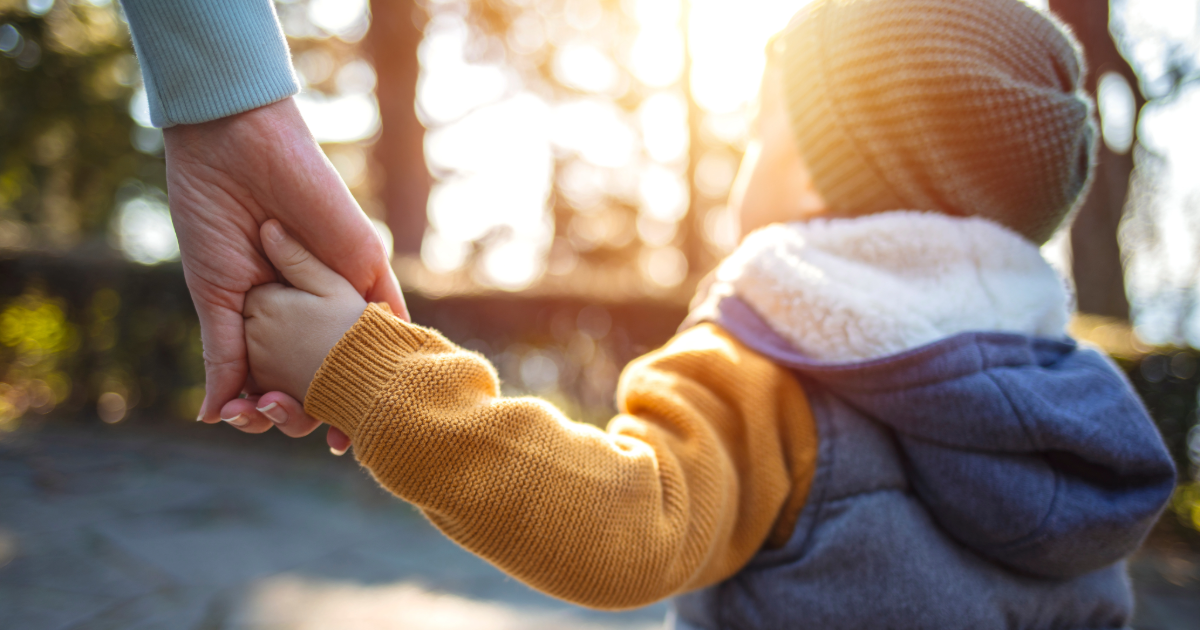 Child outdoors holding parent's hand